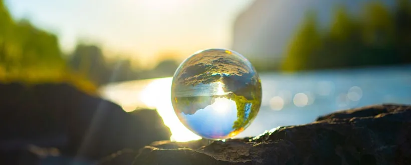 Esfera de cristal sobre una roca junto a un río, reflejando el paisaje al atardecer